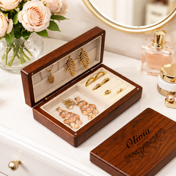 Open dark walnut jewellery box holding gold-toned jewellery beside a closed engraved lid reading Charlotte.