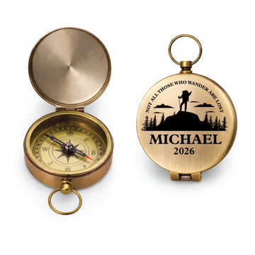 Open and closed brass compasses on a pale stone surface, with a mountain design, name and year engraved on one lid