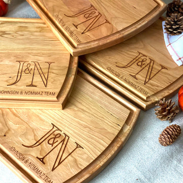 Several wooden cutting boards engraved with a J and N monogram and Johnson and Nommaz Team, arranged with pinecones.