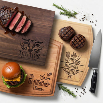 Three engraved wood barbecue cutting boards styled with grilled steak, burgers, rosemary and a chef's knife