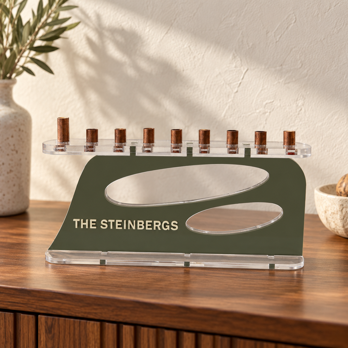 The Aperture personalized acrylic menorah in Sage and Eggshell, with THE STEINBERGS lettering, two oval openings, clear base and copper candle cups