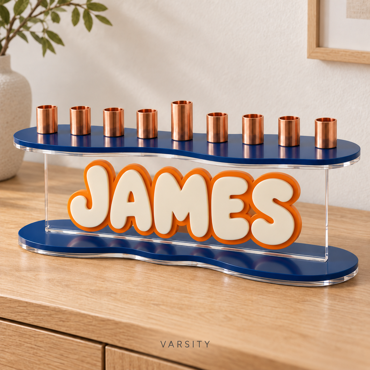 Angled view of JAMES custom acrylic menorah in Varsity, with Navy curved plates and raised Eggshell letters outlined in Orange