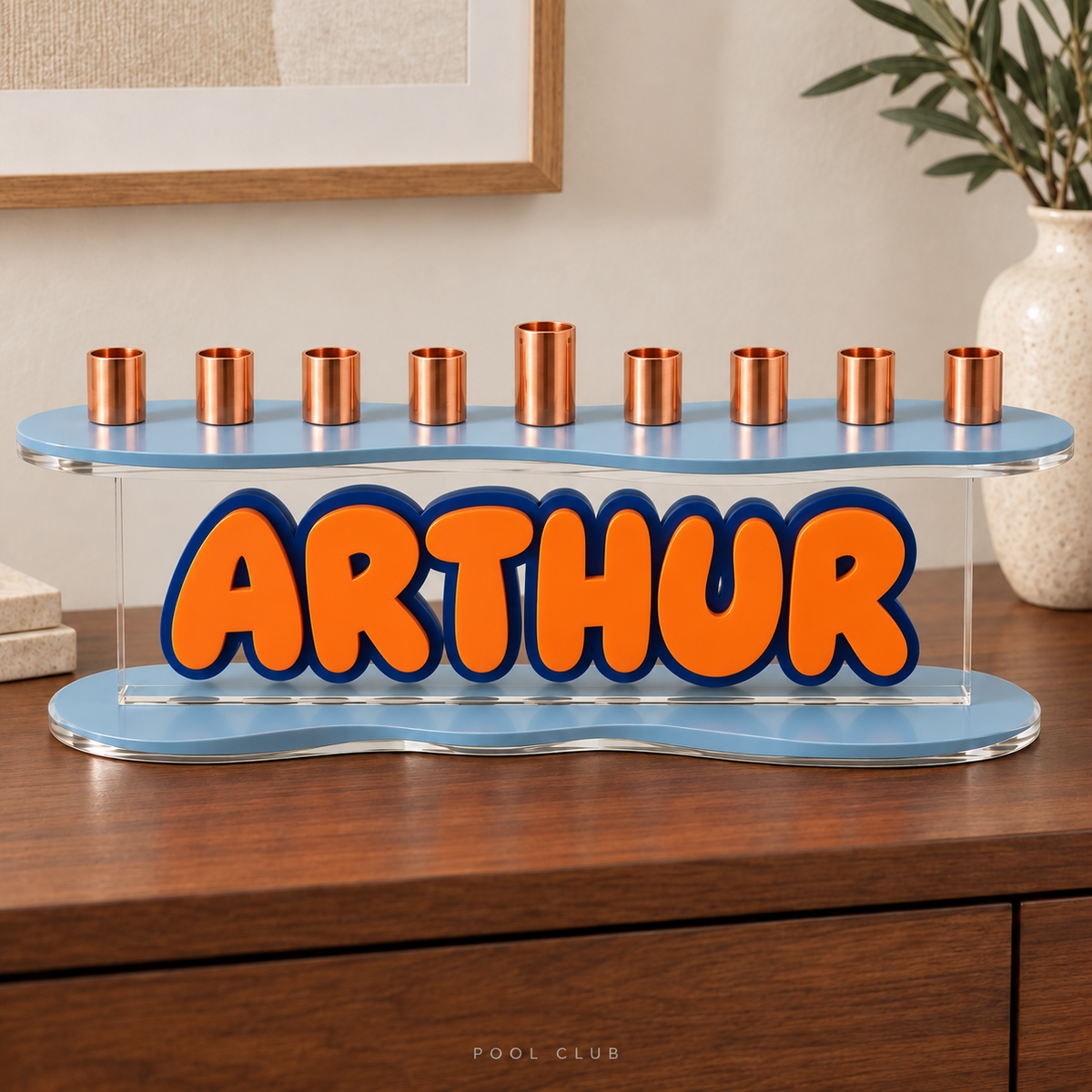 The Contour personalized acrylic menorah in Pool Club, with layered orange ARTHUR lettering and blue curved plates on a walnut console
