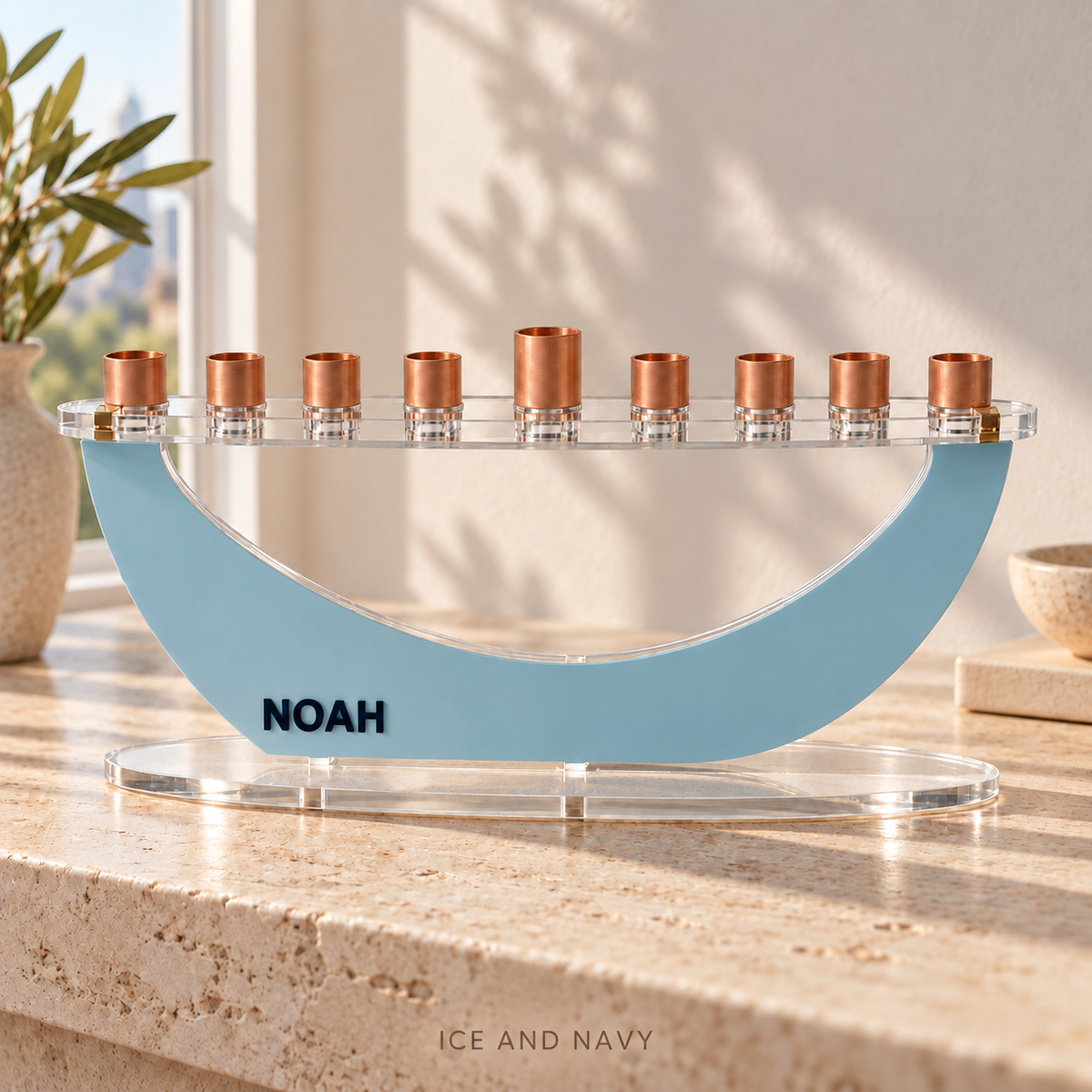 NOAH modern Crescent menorah in Ice and Navy, with raised navy letters and copper candle cups on sunlit travertine