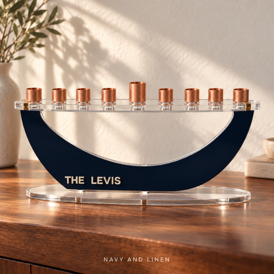 THE LEVIS personalized Crescent menorah in Navy and Linen, with raised letters, clear oval base and copper candle cups on a walnut console