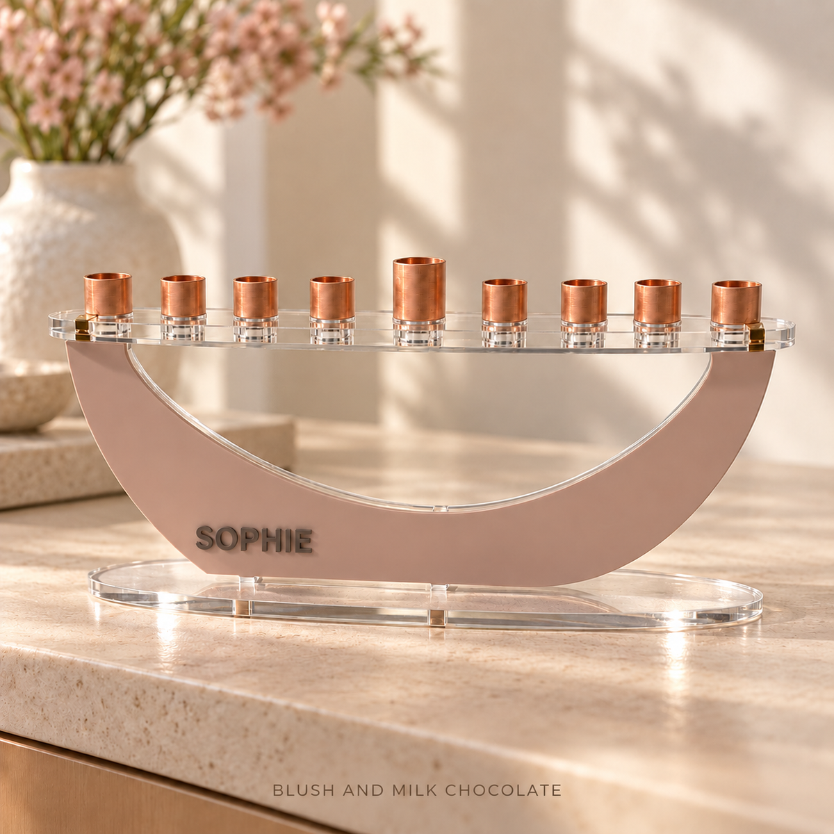 SOPHIE personalized Crescent menorah in Blush and Milk Chocolate, displayed on pale stone beside pink flowers