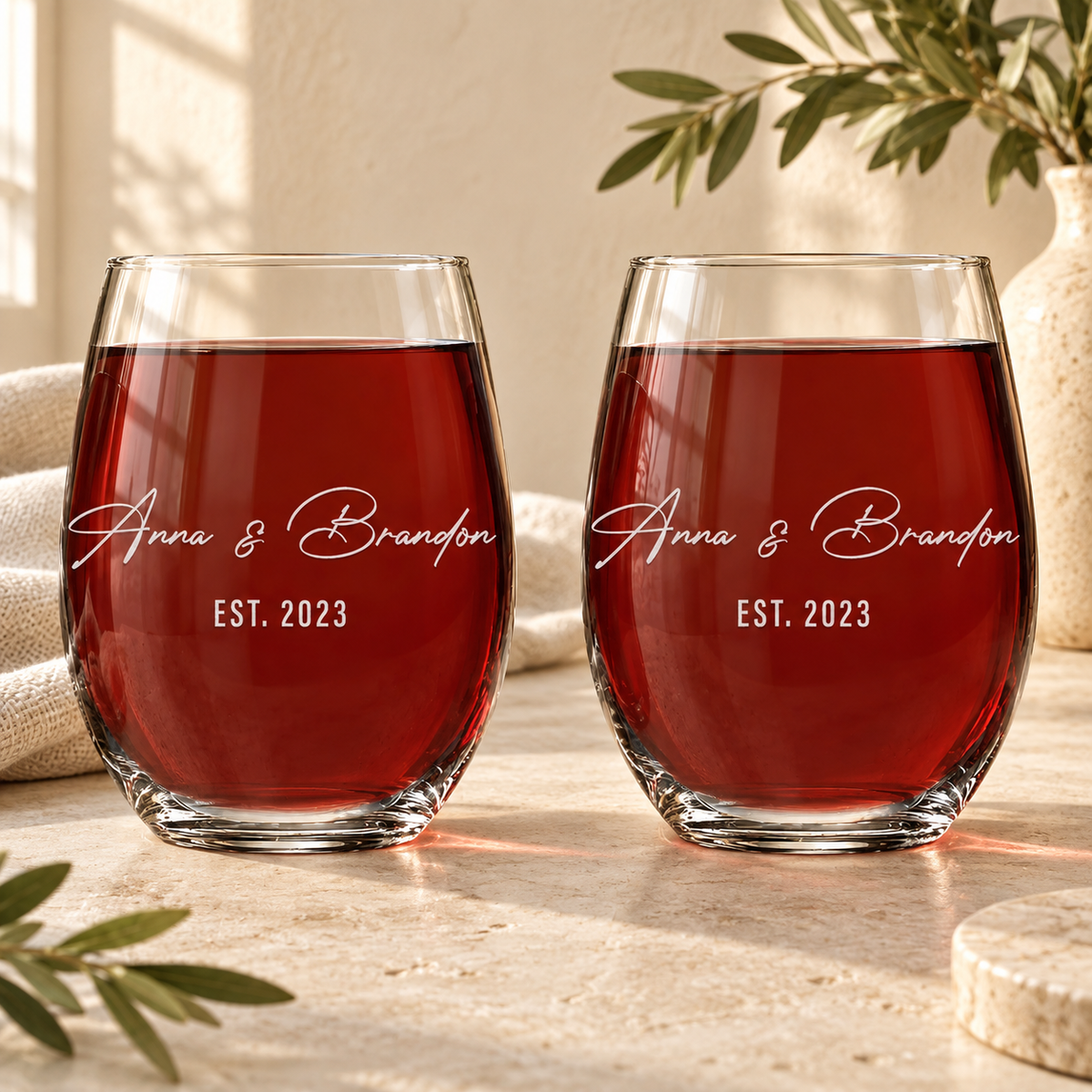A pair of personalized stemless wine glasses engraved with a couple's names and date, styled in natural daylight.