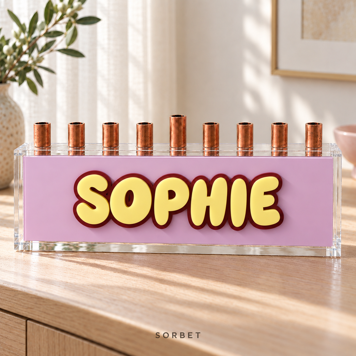 Sorbet acrylic menorah with layered yellow SOPHIE letters, a Wine outline and a Strawberry Milk pink panel on an oak console