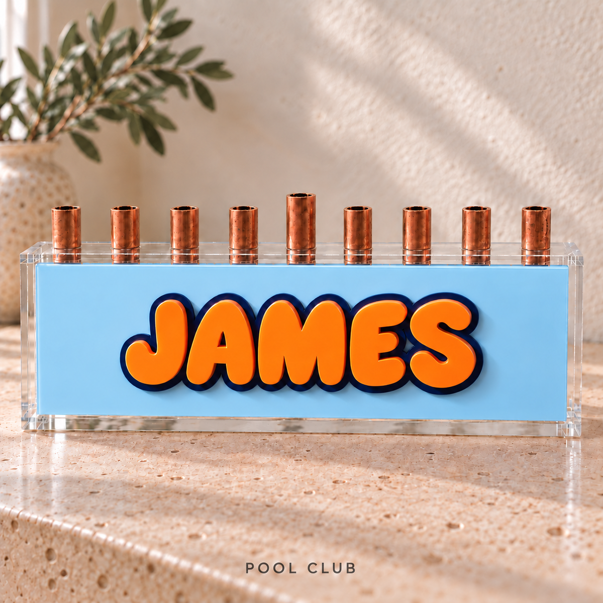 The Classic personalized acrylic menorah in Pool Club, with glossy Orange JAMES letters, Navy outlines, an Ice Blue panel and clear acrylic box.