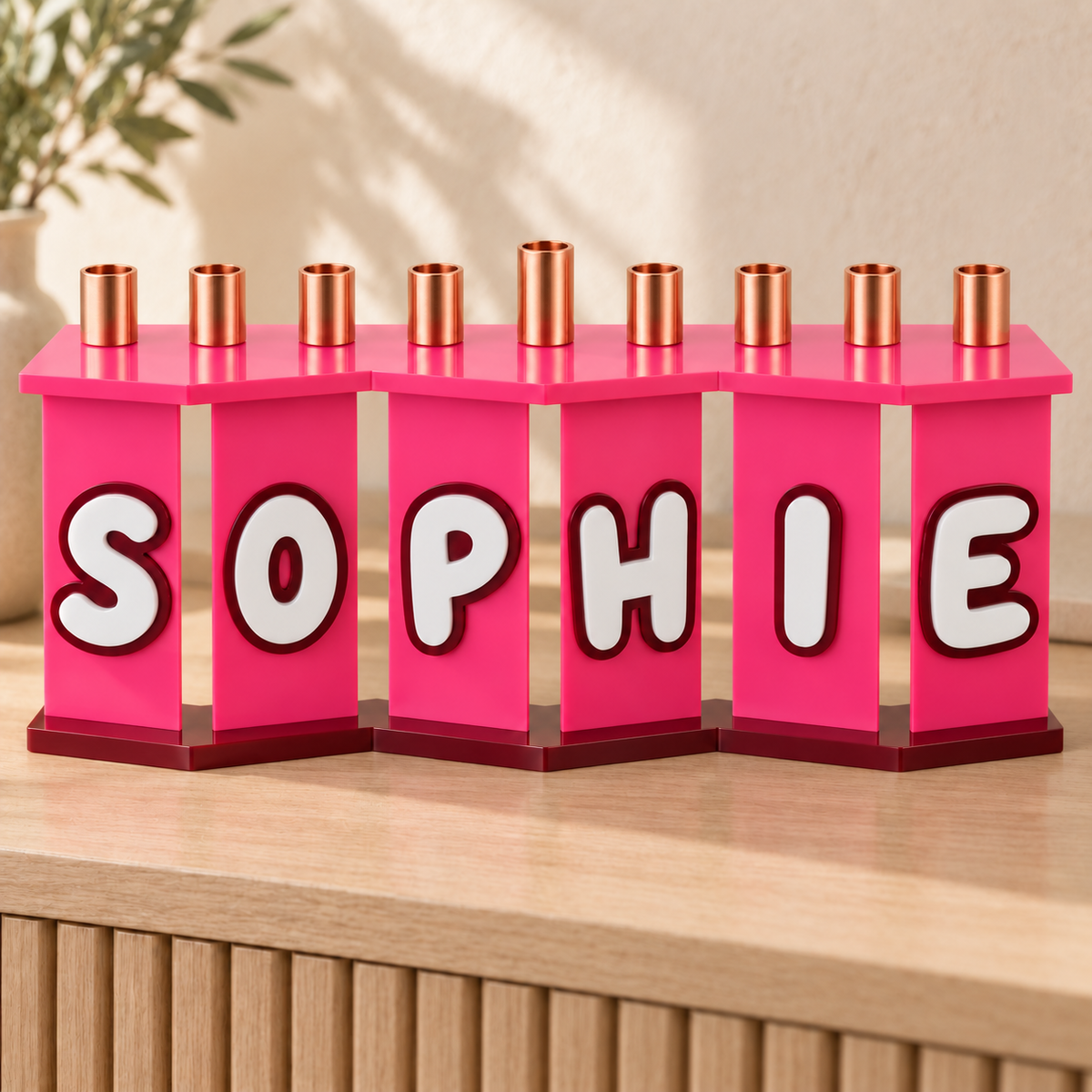 SOPHIE acrylic menorah in opaque pink with white letters and burgundy outlines on an oak console