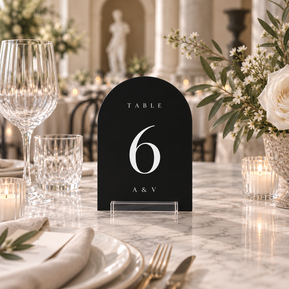 black arched acrylic wedding table number 6 with personalized initials in a clear stand on a reception table