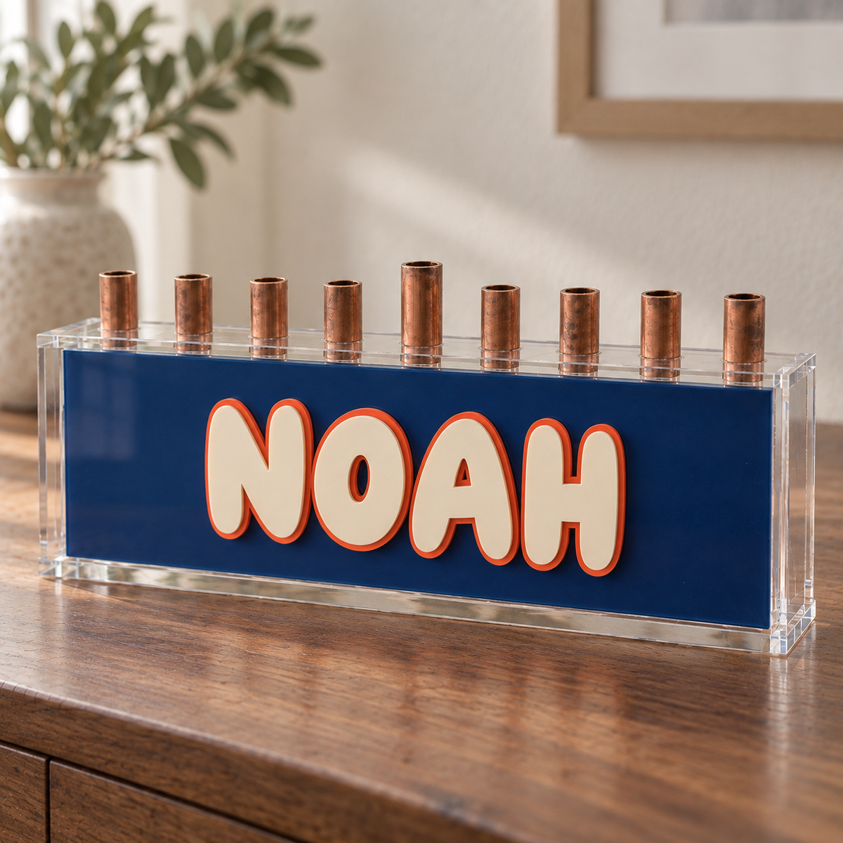 Navy Varsity NOAH menorah with cream letters and orange outline on a walnut console
