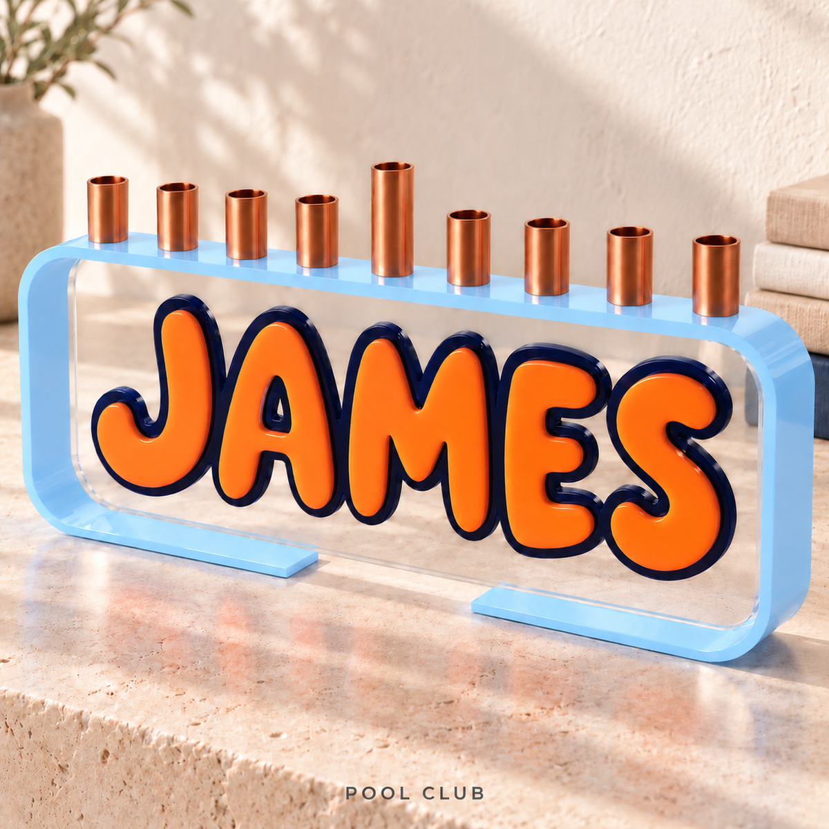 The Loop personalized JAMES menorah in Pool Club, with an Ice Blue frame, Orange letters, Navy outlines and clear acrylic front.