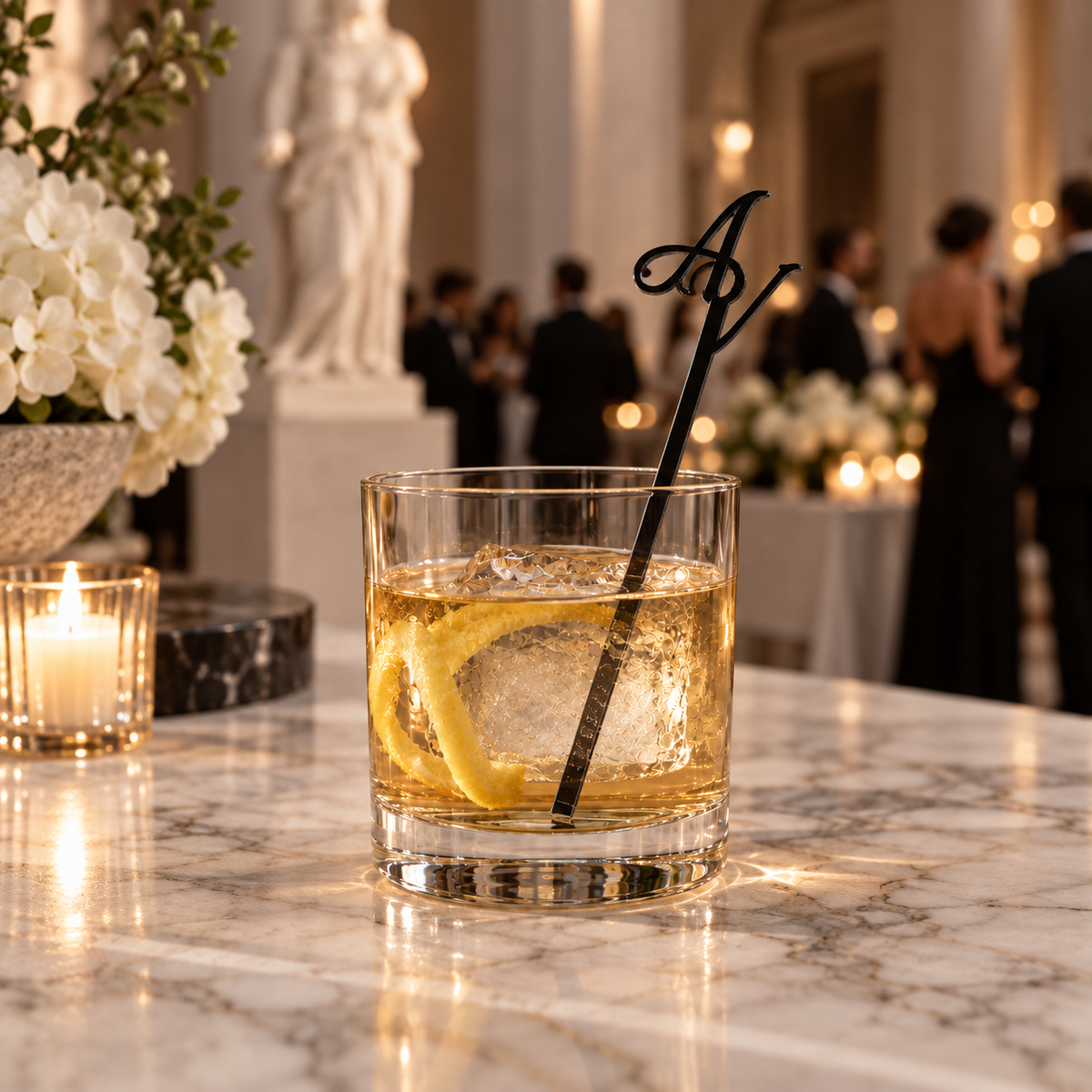 Black acrylic initial drink stirrer in an amber cocktail at a candlelit reception