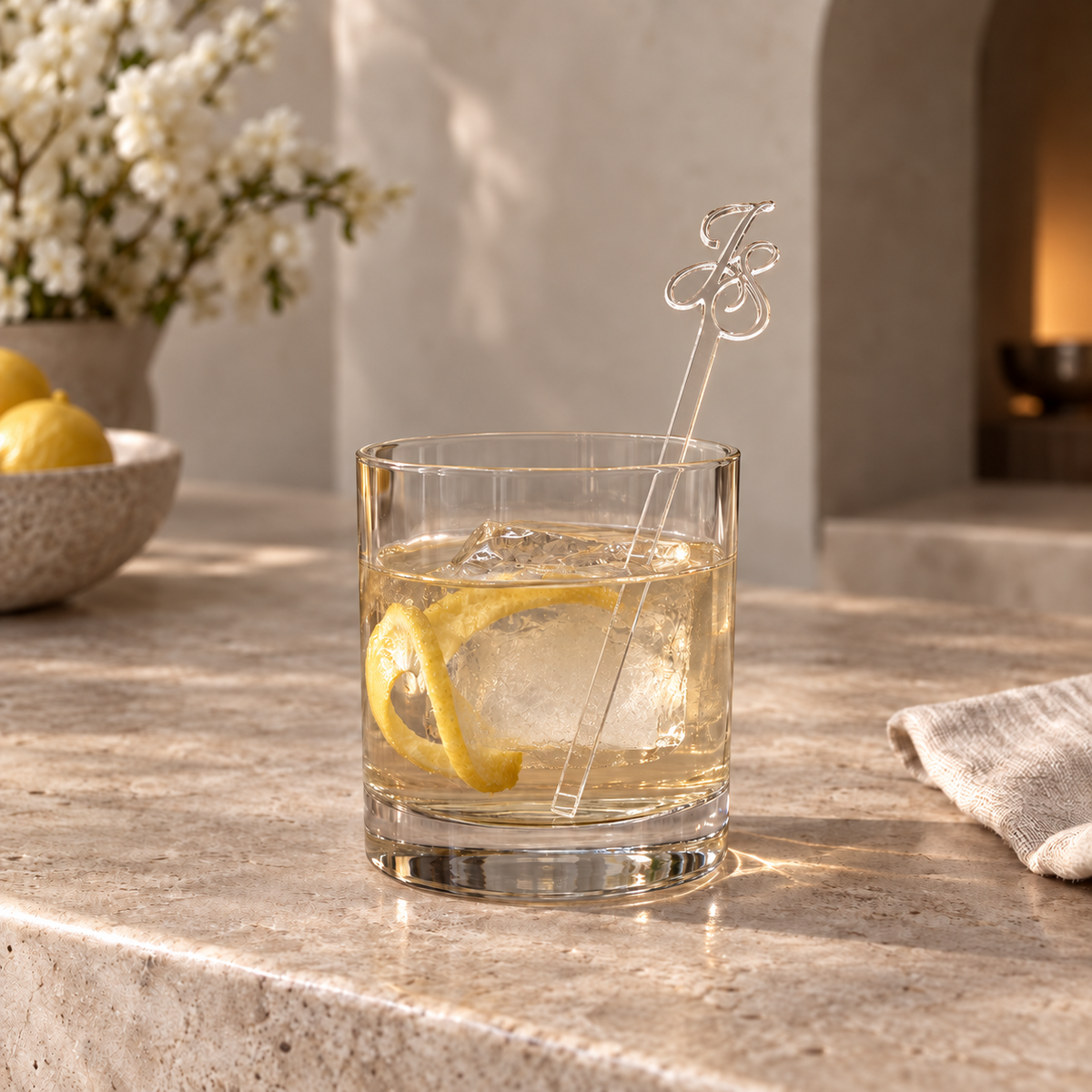 Clear acrylic drink stirrer with cutout script initials in a cocktail glass on a stone bar