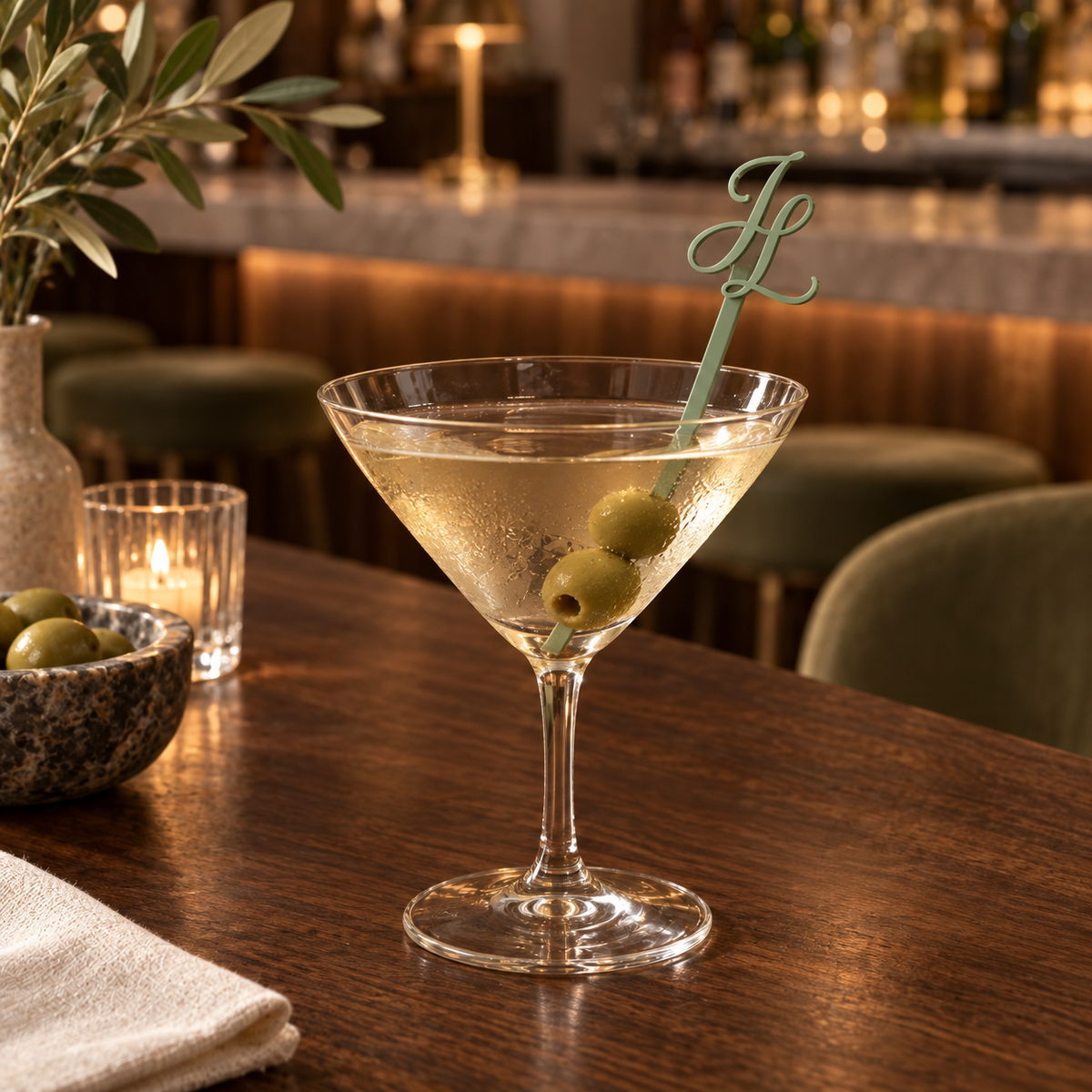 Sage acrylic monogram cocktail stirrer in a martini glass with olives at a bar
