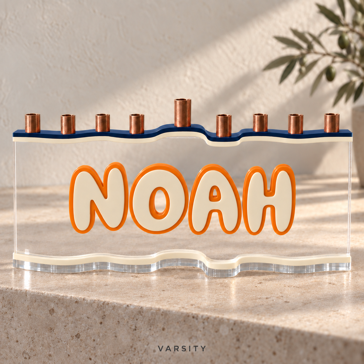 NOAH custom acrylic menorah in Varsity, with Navy deep blue top, Eggshell warm cream letters and matching base, Orange outlines and clear acrylic.